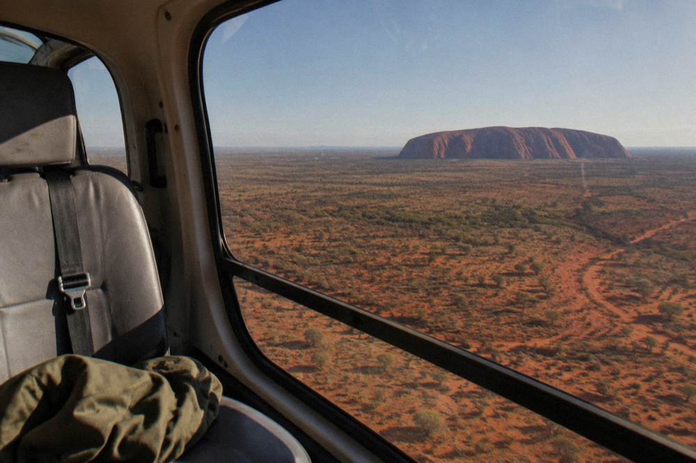 View from helicopter window showing Uluru and the desert