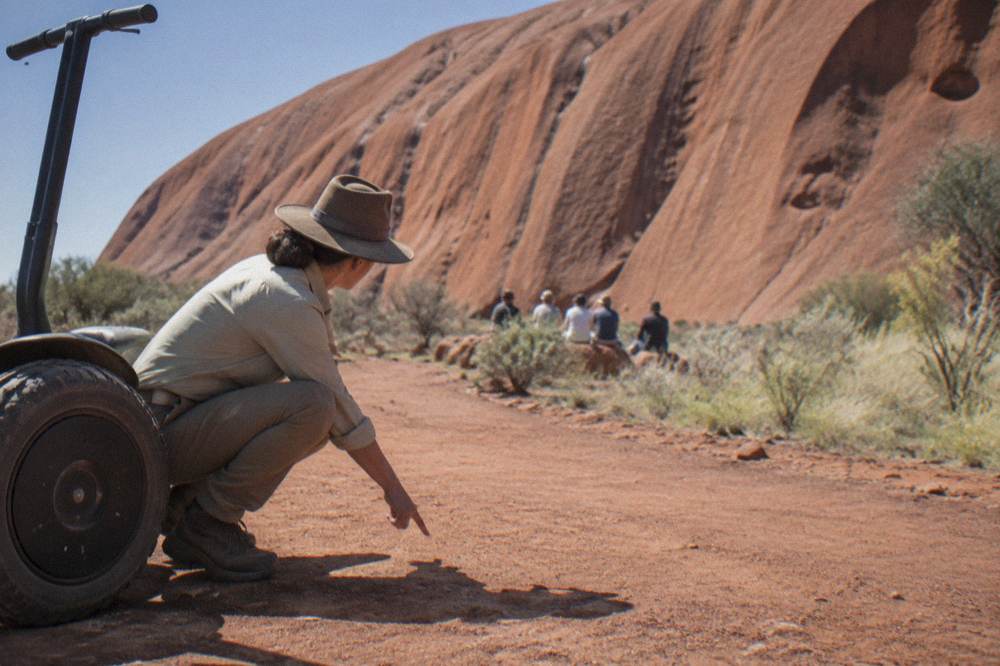 A guide speaking with a small group of walkers paused beside the rock face at Uluru