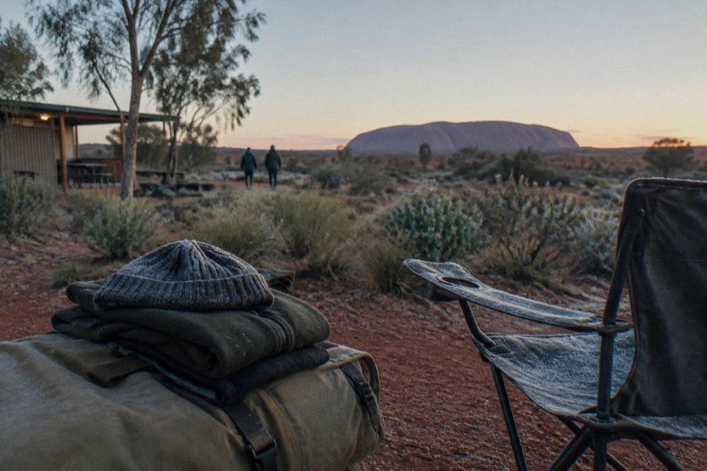 Folded warm jackets, beanie and backpack on a bench at a desert campground at dawn