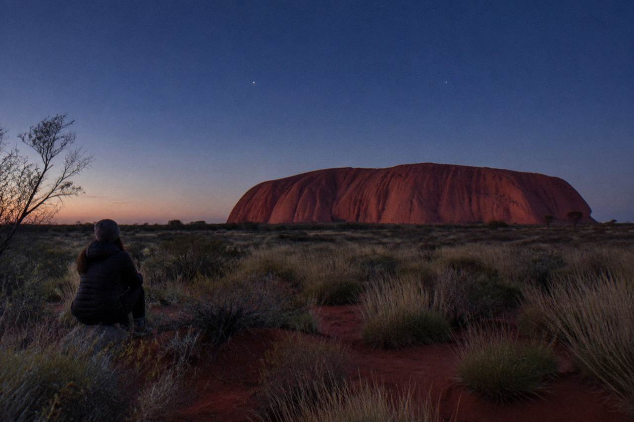 Uluru under a deep blue twilight sky with red desert sand cooling in the evening