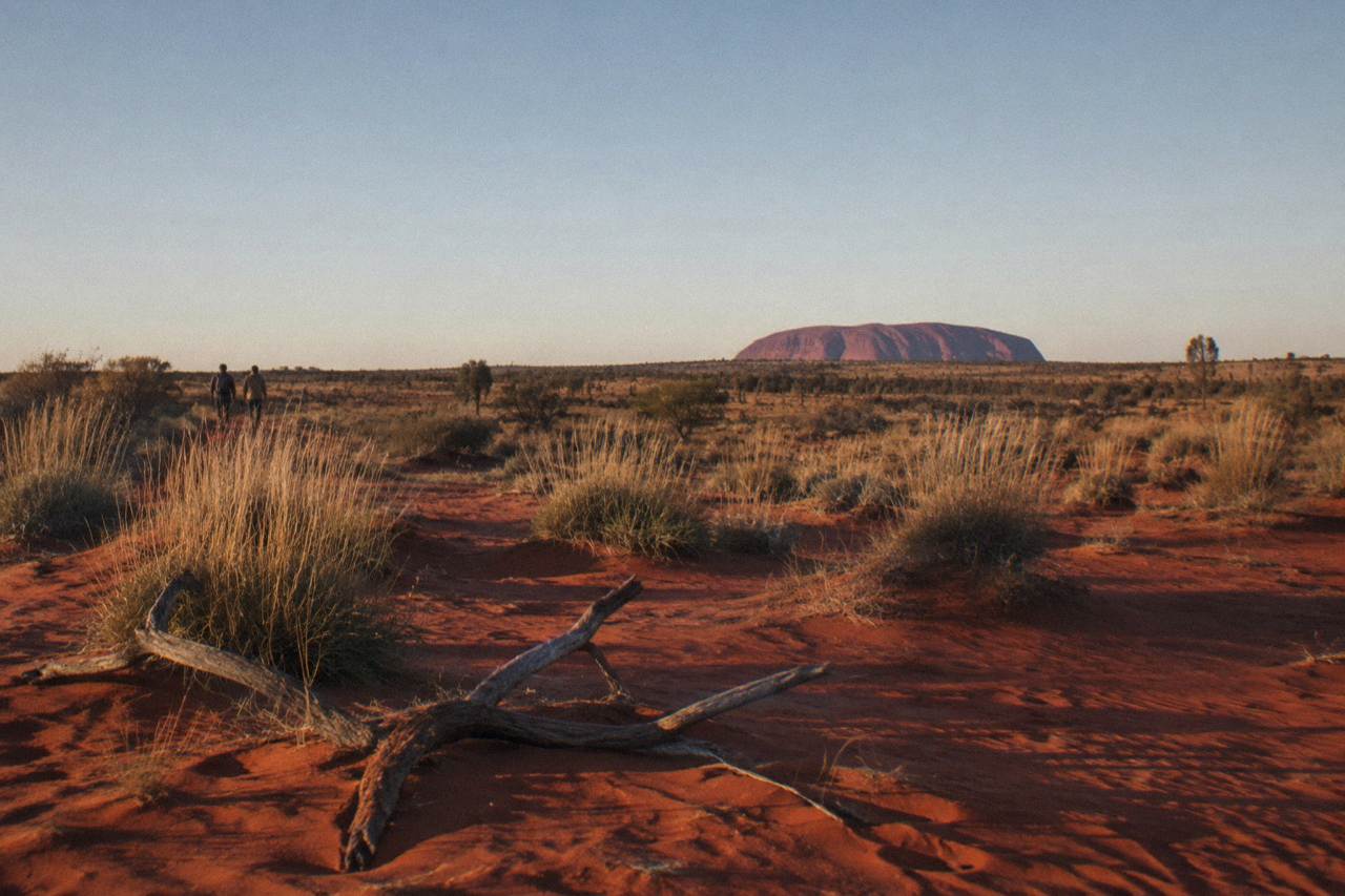 Red desert plain with Uluru rising in the distance under a wide sky