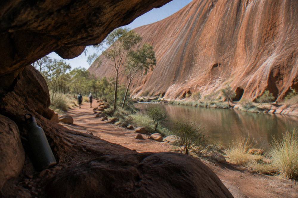 Small group of walkers on a red dirt path beside the base of Uluru