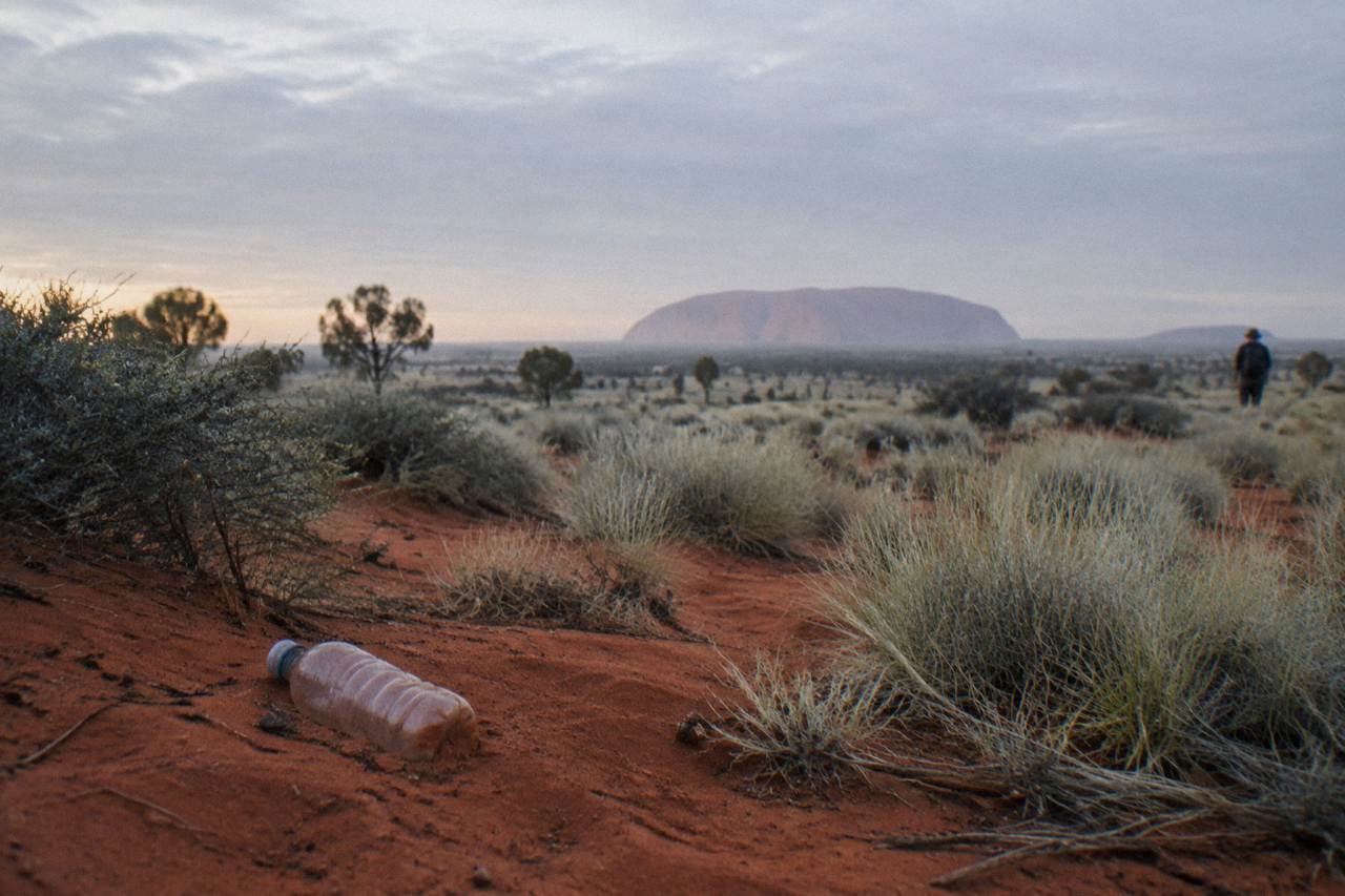 Red desert plain with Uluru rising in the distance under a pale morning sky