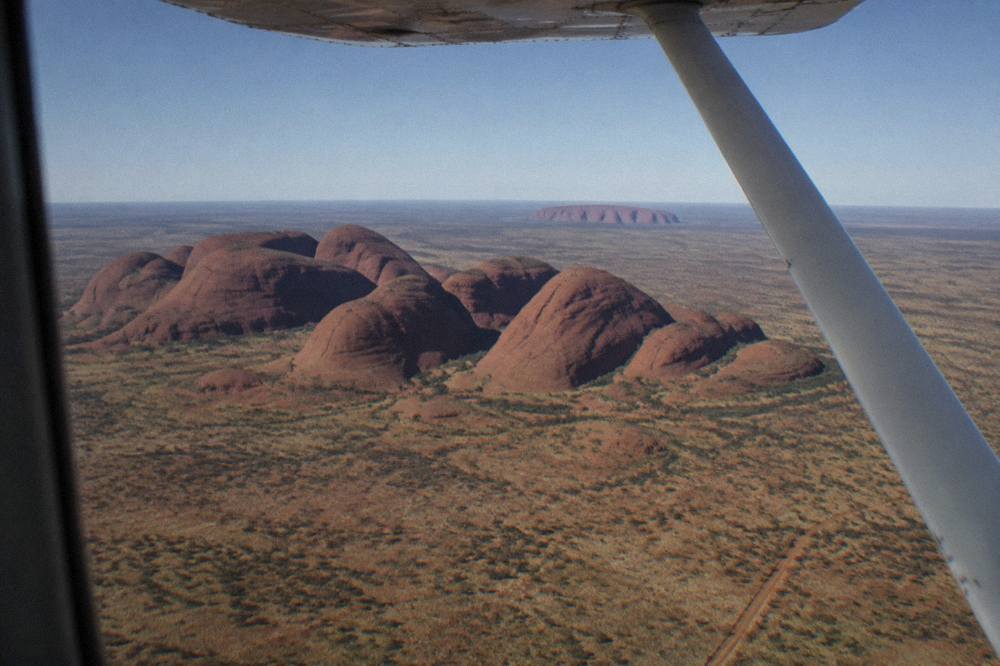 Aerial view of Uluru and Kata Tjuta from a plane window, red desert landscape, clear morning sky