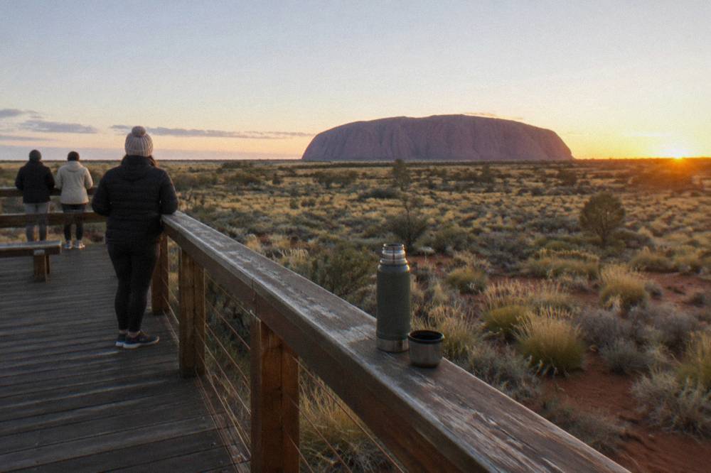 A raised timber viewing platform looking across open desert toward Uluru in early morning light