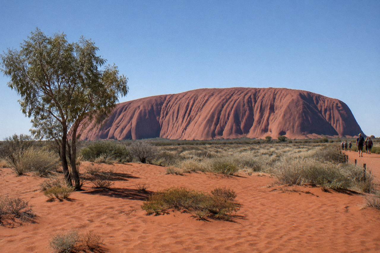 Uluru rising above red sand and low desert scrub under a wide open sky