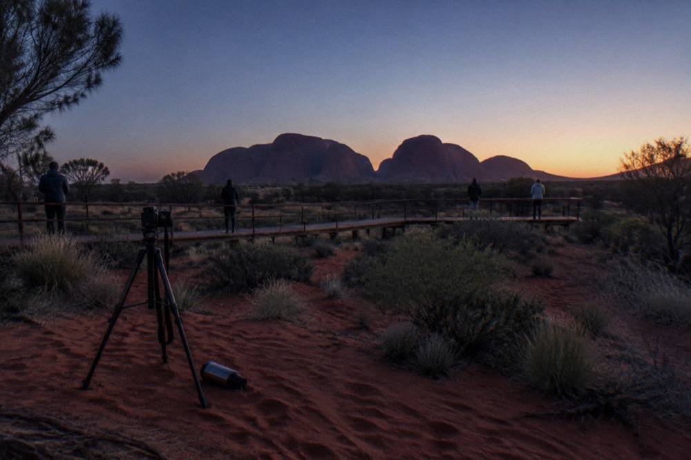 Viewing platform at dawn with visitors spread out watching colour build over distant desert domes