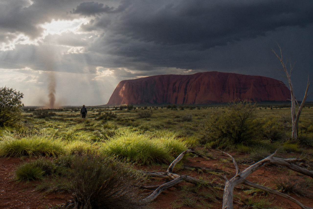 The red sandstone walls of Uluru rising above desert plain and spinifex under a wide sky