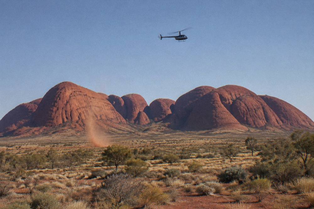 Helicopter in flight above the red rock domes of Kata Tjuta under clear sky