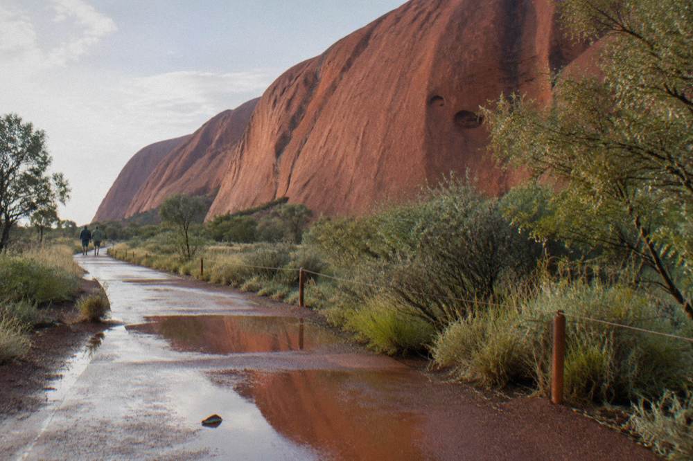 Gentle paved path along the base of Uluru with low desert shrubs on either side