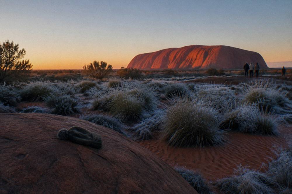 Sunrise light striking the flanks of Uluru seen from a sandy viewing dune