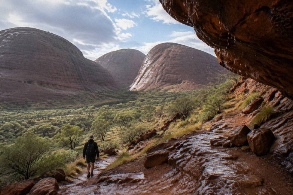 Rugged red domes of Kata Tjuta rising above a dry gorge floor dotted with green shrubs