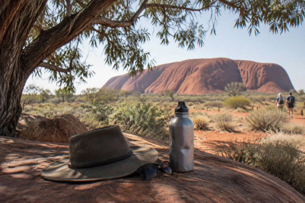 A wide-brimmed hat, sunglasses and a water bottle resting on a bench under bright desert sun