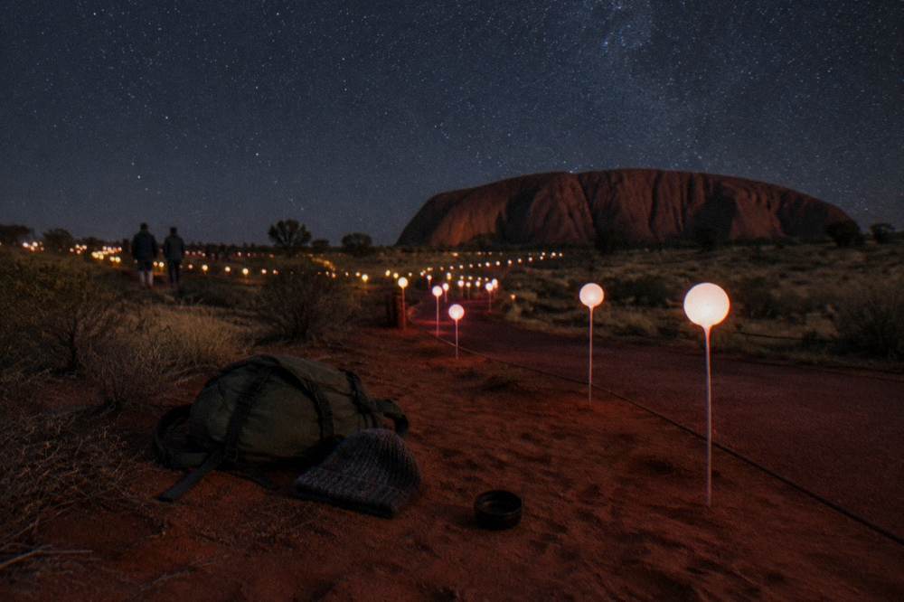 A packed day pack and jacket beside a pathway of glowing coloured spheres at night