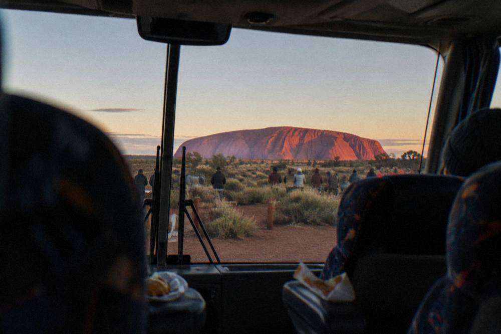 A large red sandstone monolith glowing at dawn above open desert plain