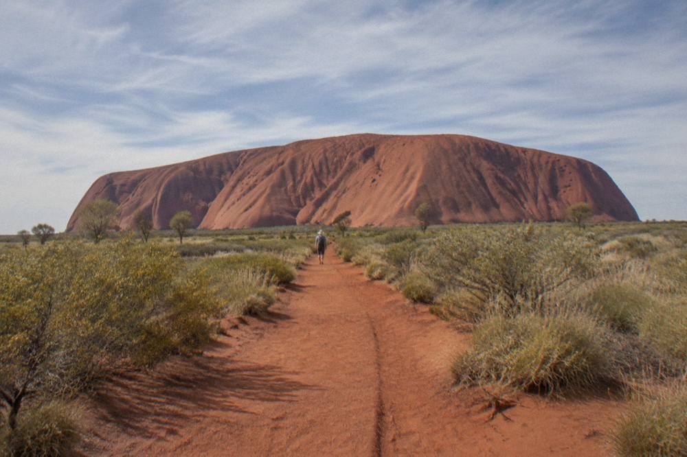 Long red dirt path leading toward the base of Uluru under a wide open sky