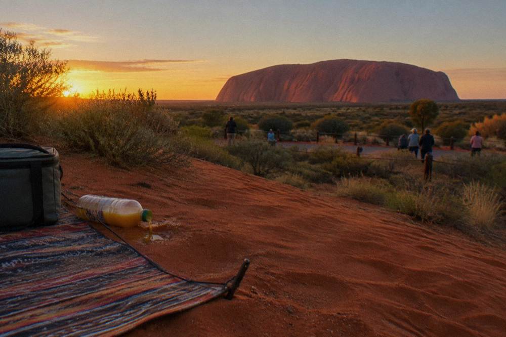 Simple picnic setup on a sandy rise overlooking Uluru at golden hour