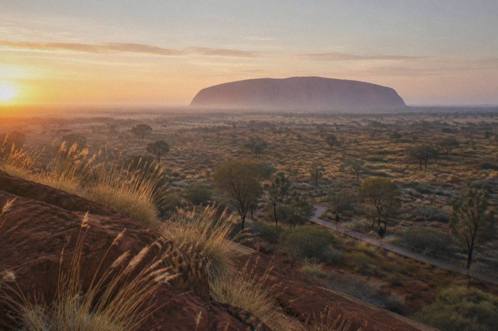 A distant view of Uluru's rounded profile against a pale morning sky