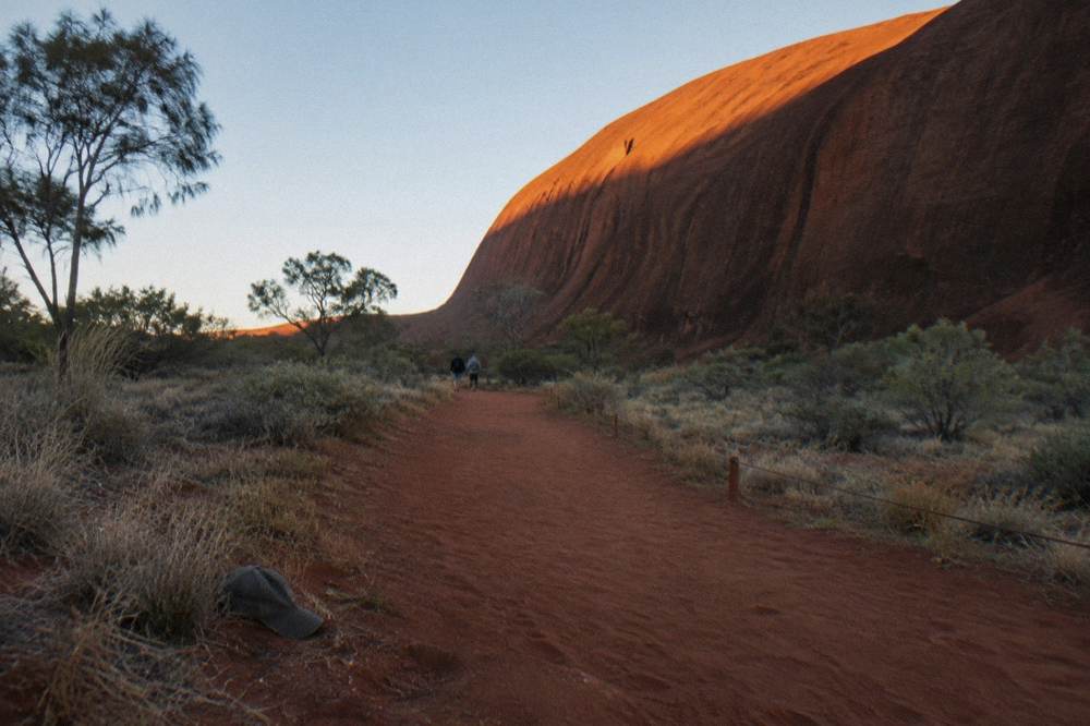 Walkers on the red dirt track of the Uluru base walk with the rock wall on one side