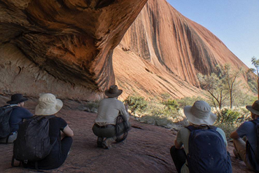 Ranger talking to a small group at the base of Uluru near a rock overhang