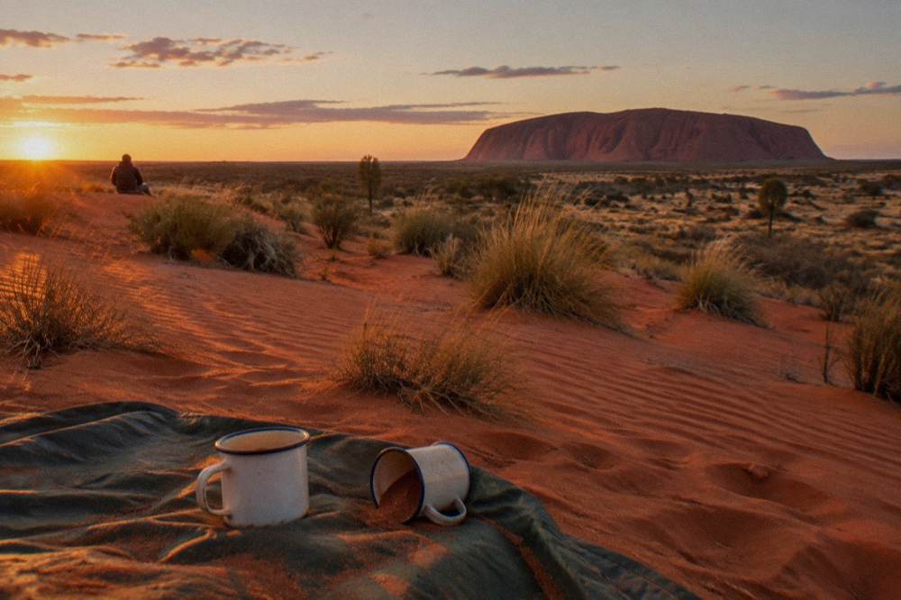 Red sand dune with spinifex grass and a distant view of Uluru at sunset