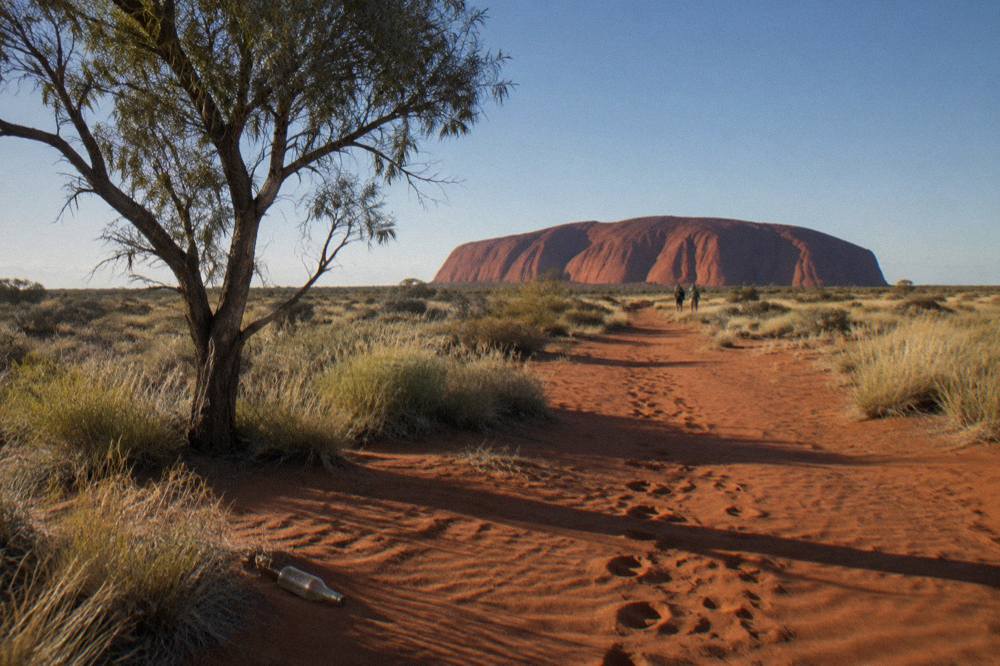 Red desert sand and low scrub under a clear blue sky near Uluru