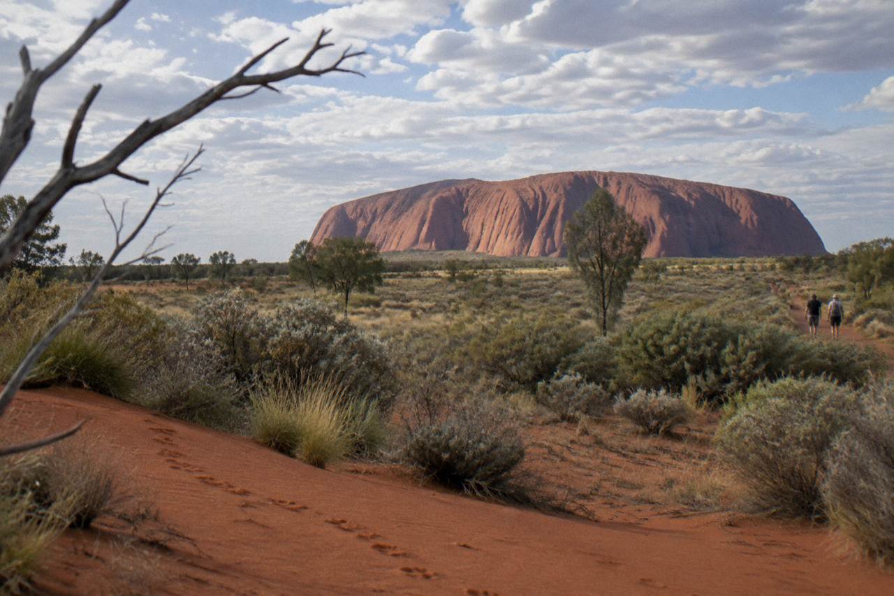 Uluru rising above red sand plain under a wide morning sky