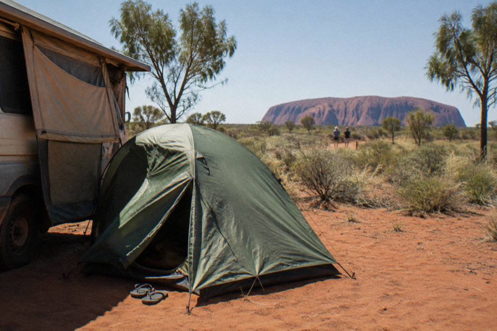 Tent pitched on red sand beside a campervan at a desert campground