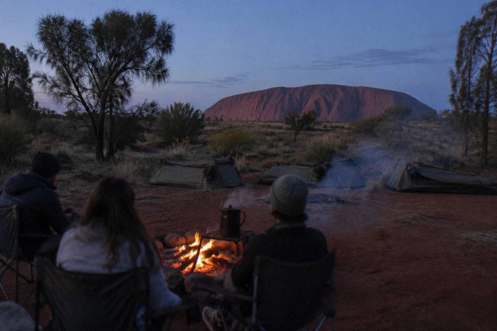 Campers seated around a fire with swags laid out on the red earth