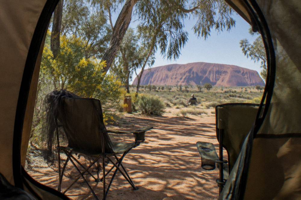 Tent and camping chairs on pale sand with desert oaks in early morning light