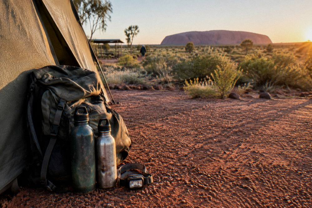 Backpack and water bottles resting beside a tent flap at sunrise