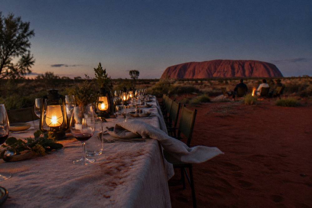 Long table set for an outdoor dinner in red desert sand with lanterns