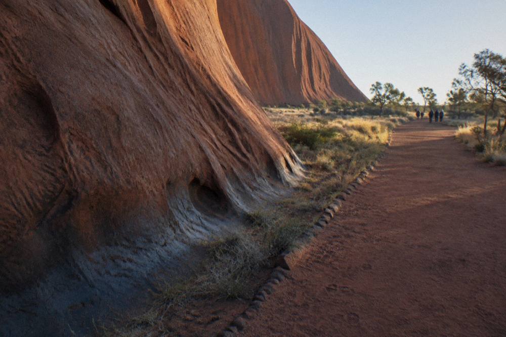 A marked walking track beside a low rock face at the base of Uluru in early morning light