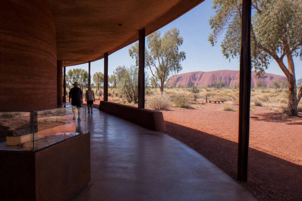 A low desert building with shaded walkways and interpretive displays near the base of Uluru