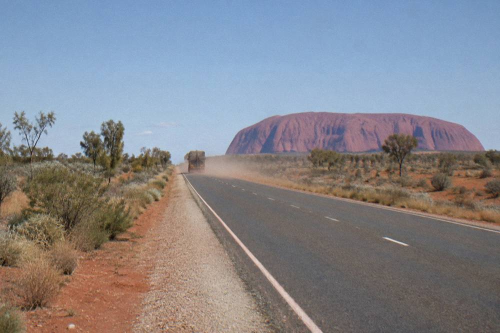 A sealed outback highway cutting straight through red dirt country toward the horizon