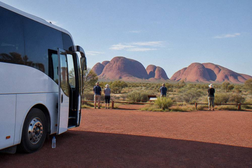 A touring coach parked at a desert lookout with red rock formations in the distance