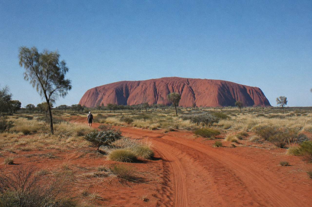 Red desert plain stretching toward Uluru under a wide blue sky near Yulara