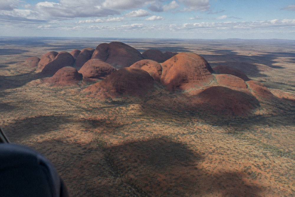 Aerial view of the Kata Tjuta dome cluster spread across red desert plains under scattered cloud