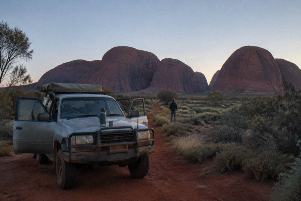 Tour vehicle parked on a red dirt road beside domed rock formations at dawn