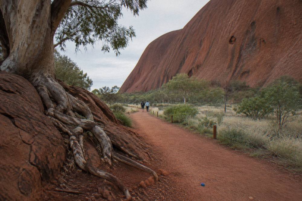 A red dirt walking track curving along the base of Uluru beneath tall rock walls