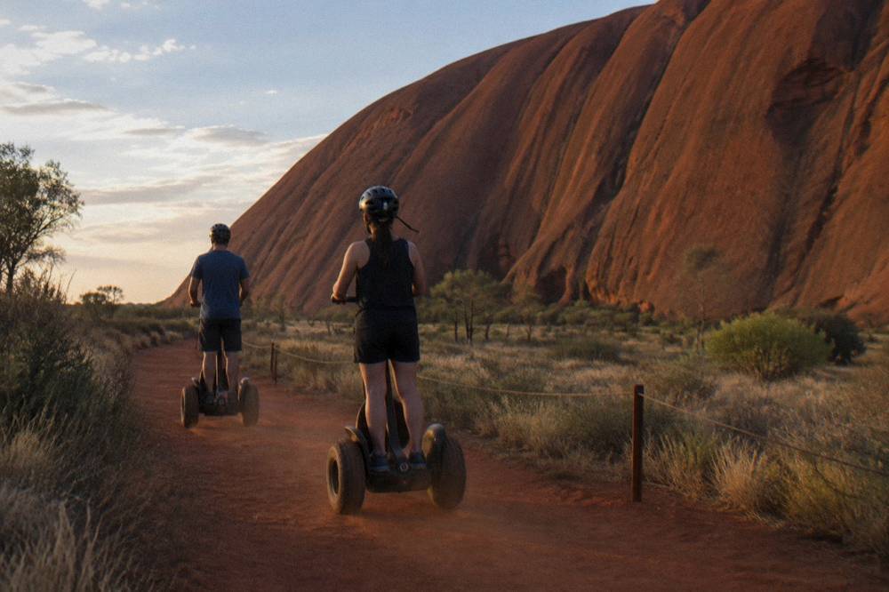 A small group of Segway riders travelling along a red dirt path beside tall rock walls