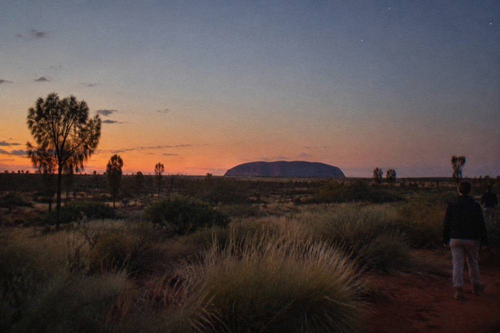 A wide desert plain at dusk with a large sandstone monolith silhouetted on the horizon