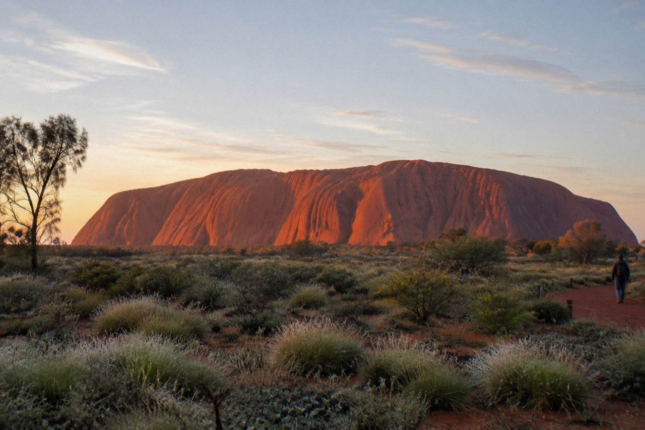 Uluru rock face glowing red under an open desert sky at dawn