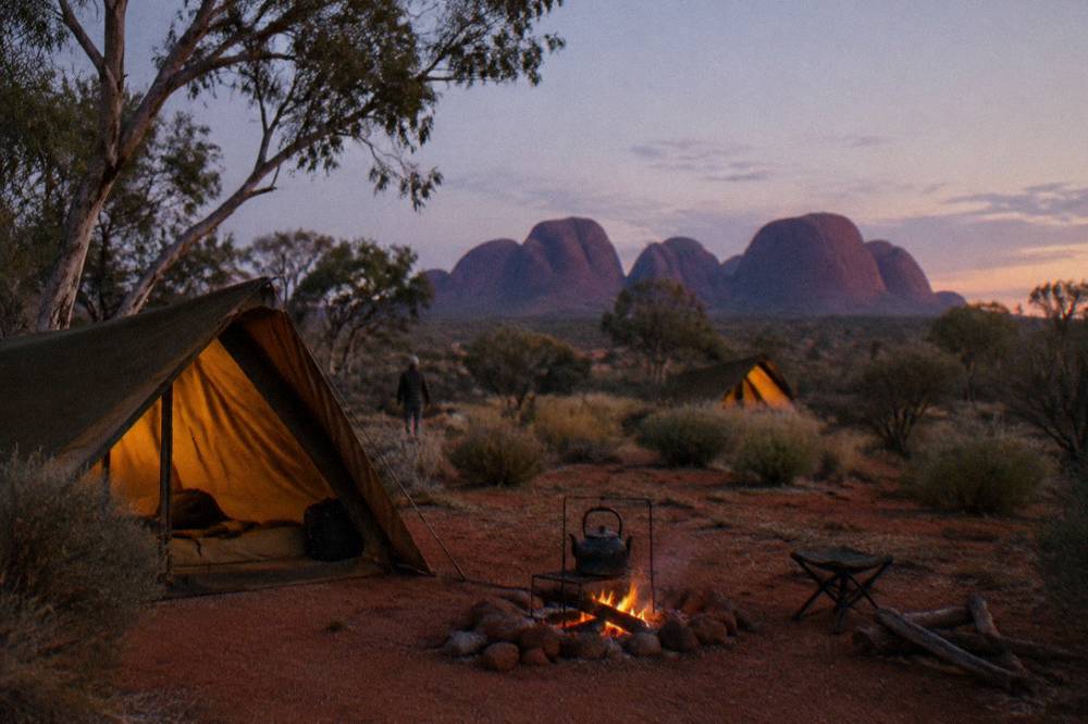 Canvas tents and campfire set up on red earth among desert oaks at dusk
