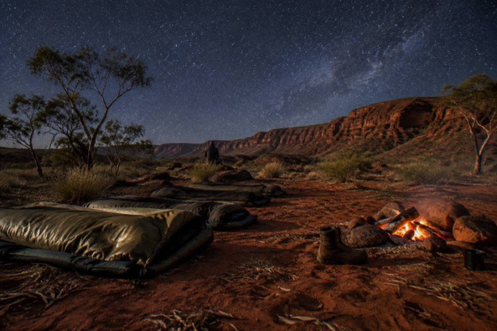 Swags laid out beside a campfire under a star-filled desert sky