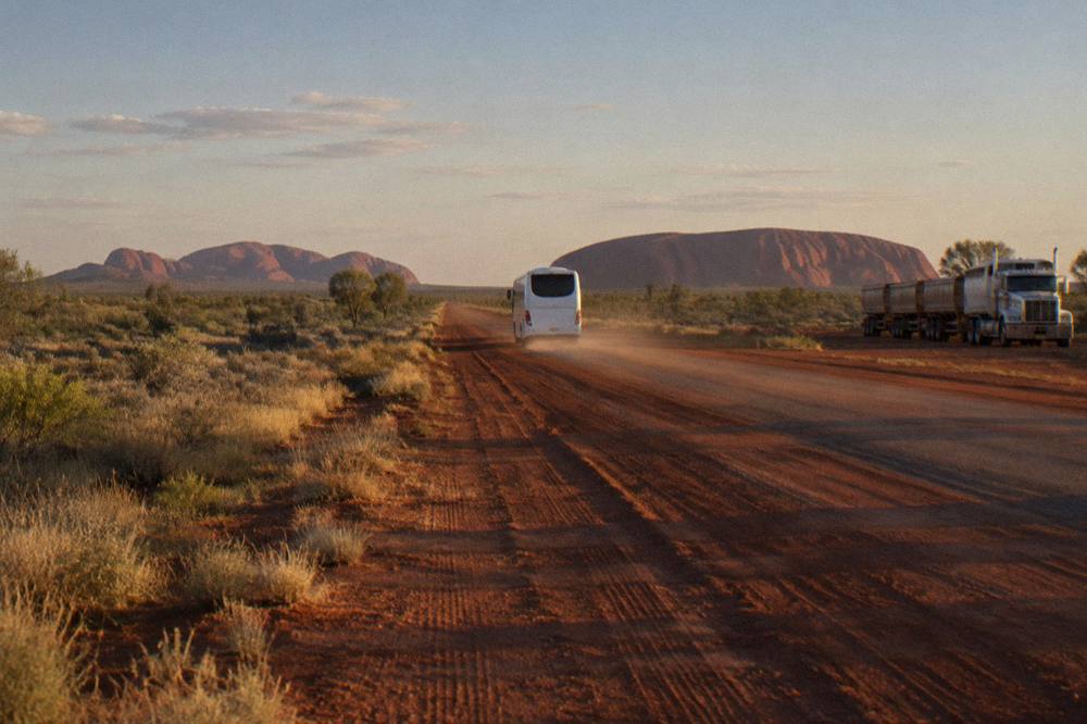 Coach travelling a straight red-dirt highway toward distant rock formations