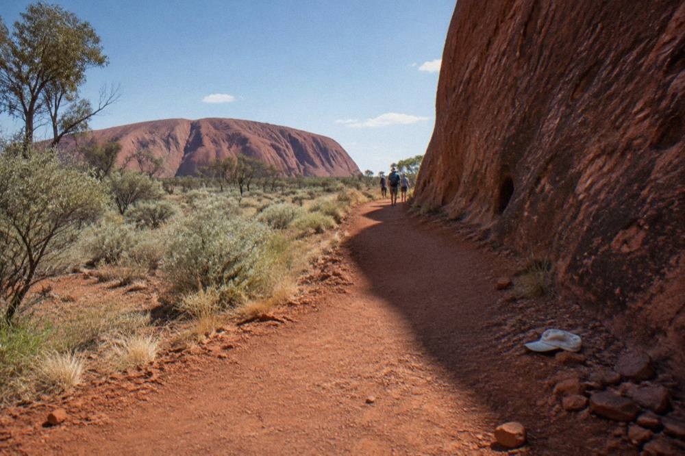 Flat red earth walking path curving alongside the base of a tall rock wall