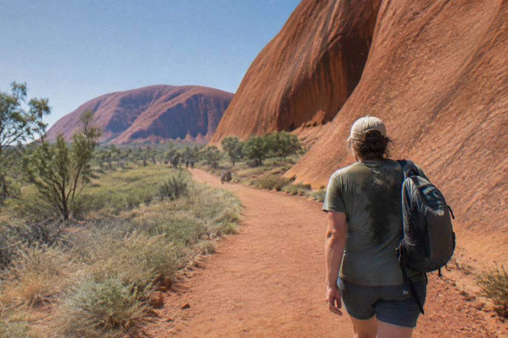 Walker carrying a daypack on a wide dirt track beside smooth curved rock walls in morning light