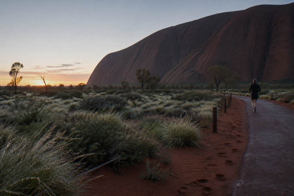Smooth path curving along the base of Uluru through open desert scrub