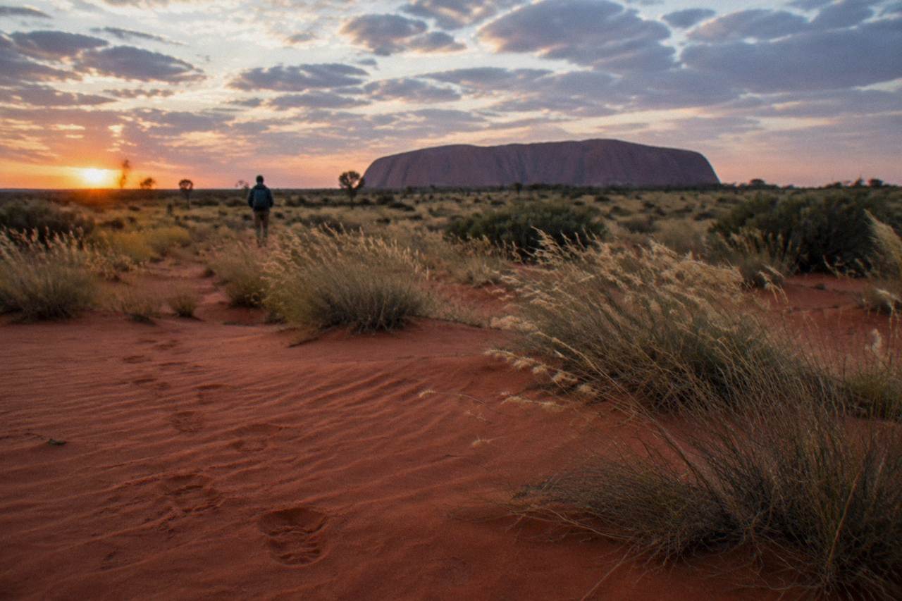 Red desert sand stretching toward Uluru under a wide evening sky